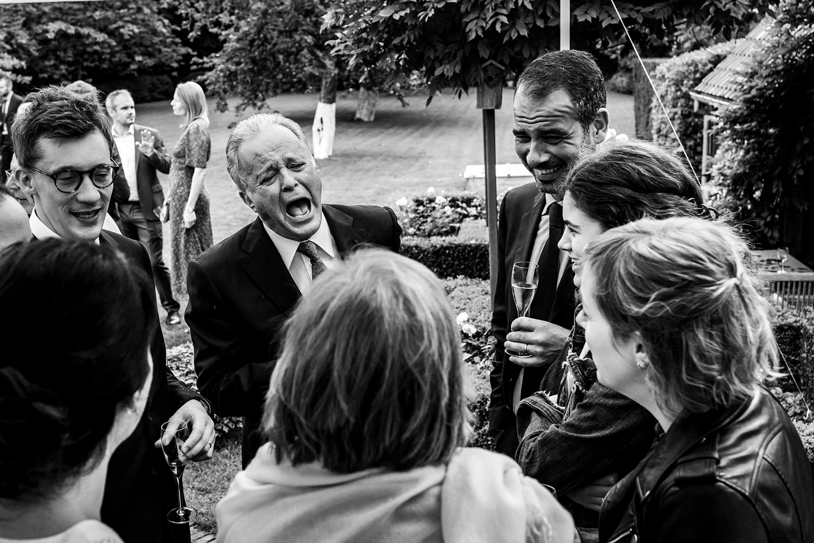 Le papa de la mariée éclate de rire dans un groupe debout lors d'une réception de mariage dans le Brabant Wallon.