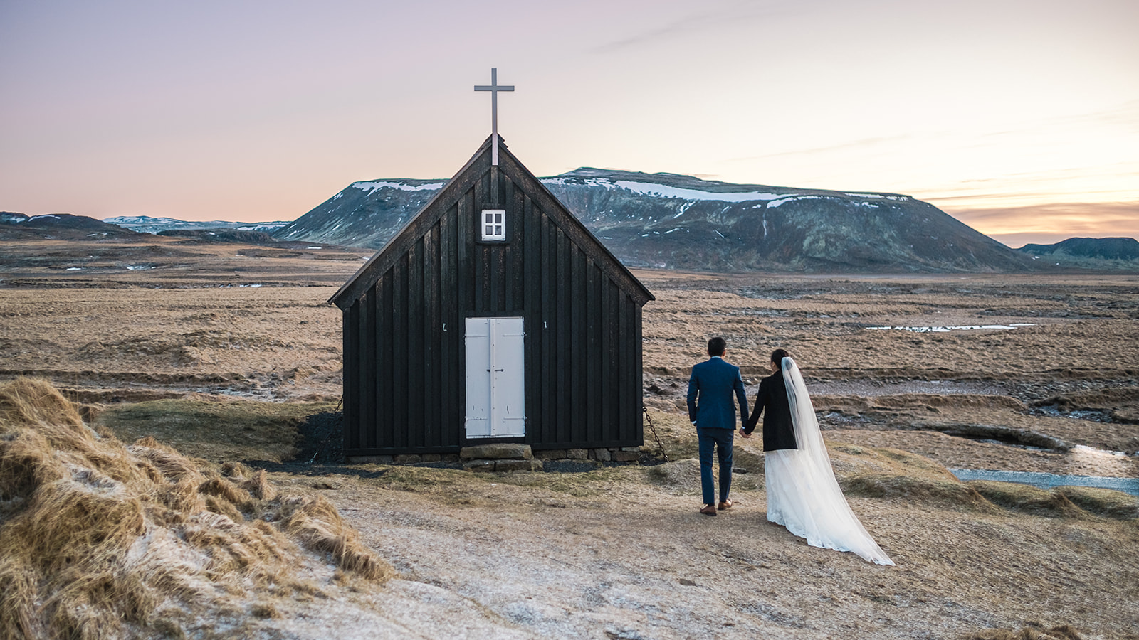 Bride and groom standing in front of Krýsuvík Black Church in Iceland in winter