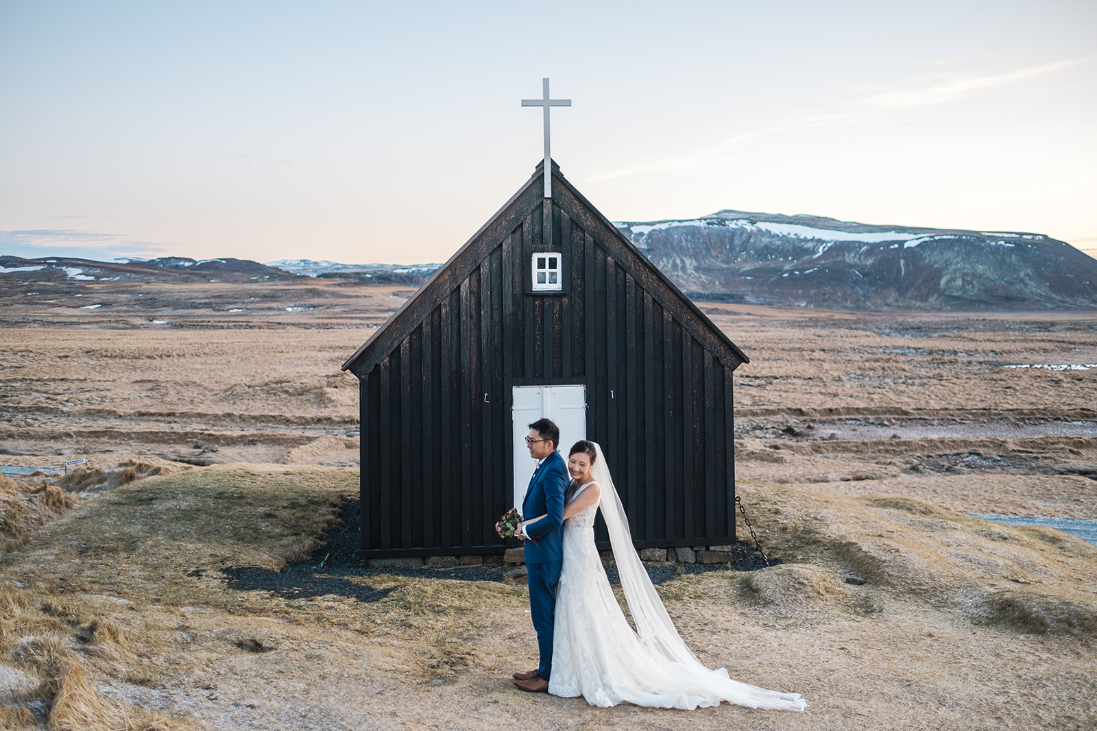 Stunning bride and groom standing in front of Krýsuvík Black Church in Iceland in winter