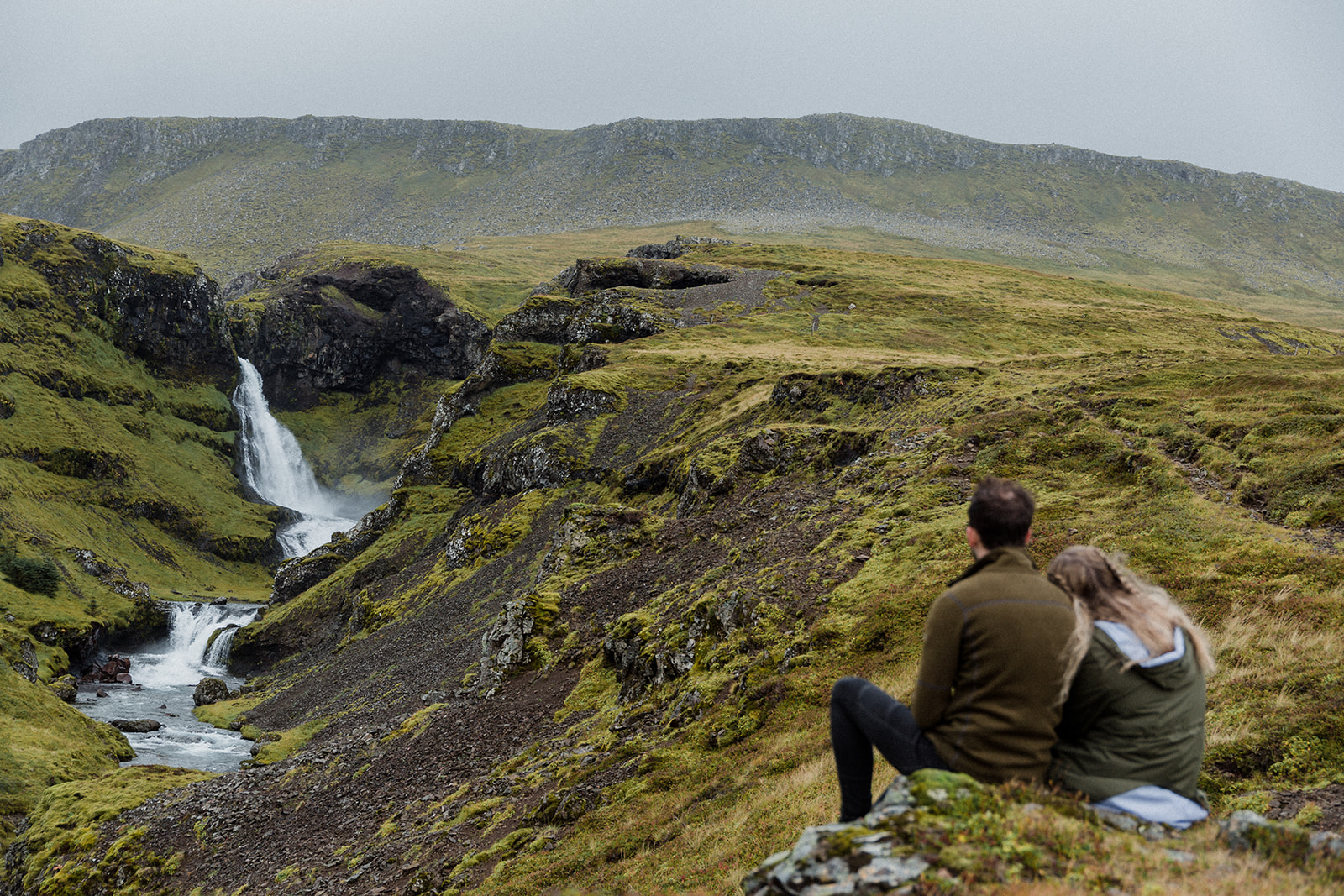 A couple sitting in front of a stunning waterfall enjoying an adventure session photography in Iceland