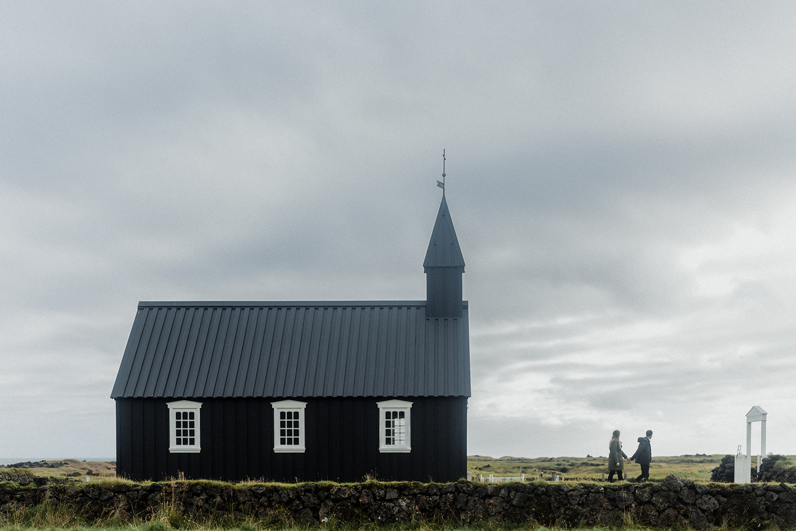 A couple standing in front of Budir black church in Iceland at the Snaefellsnes Peninsula.