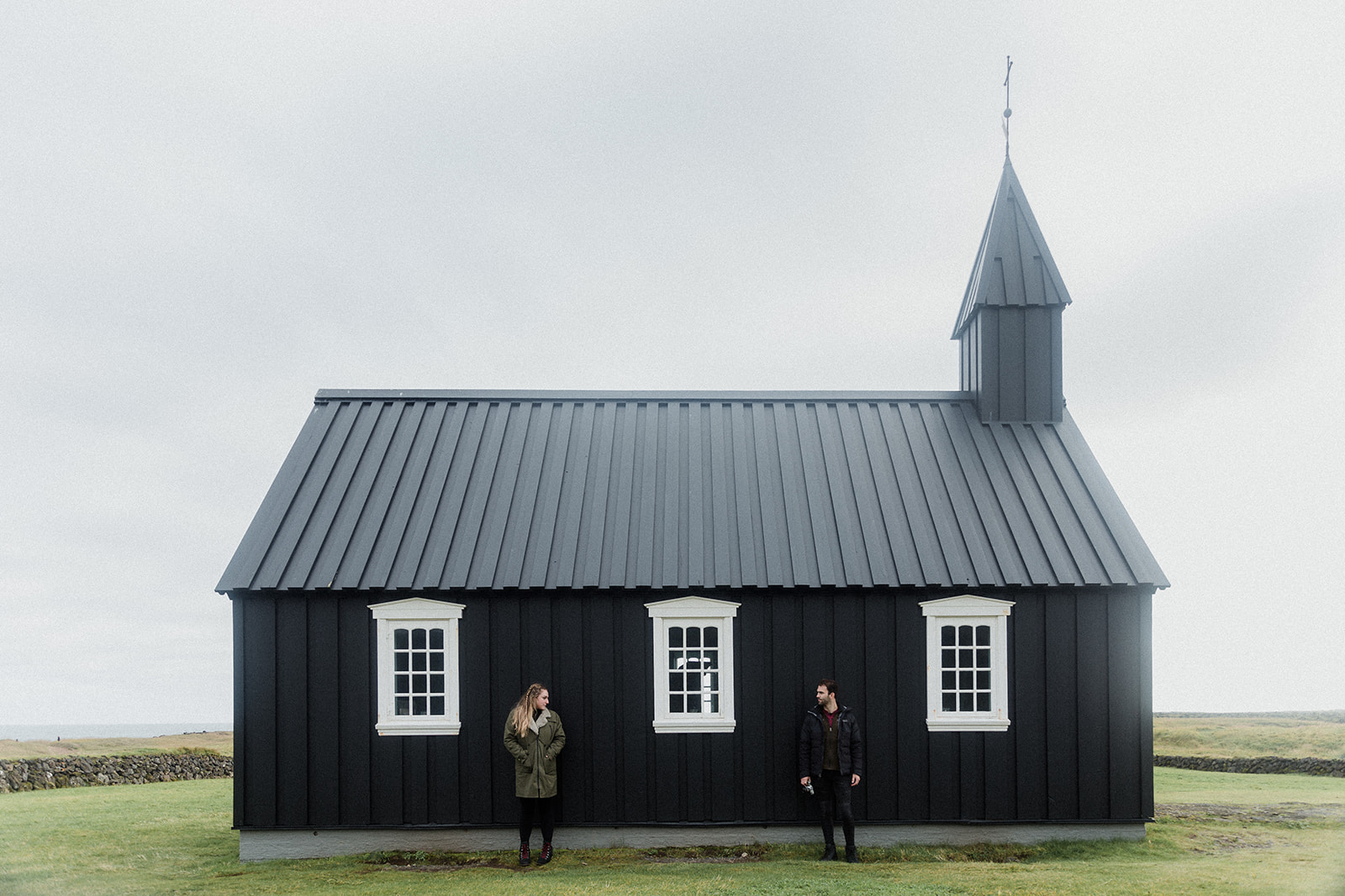 A couple standing in front of Budir black church in Iceland at the Snaefellsnes Peninsula.