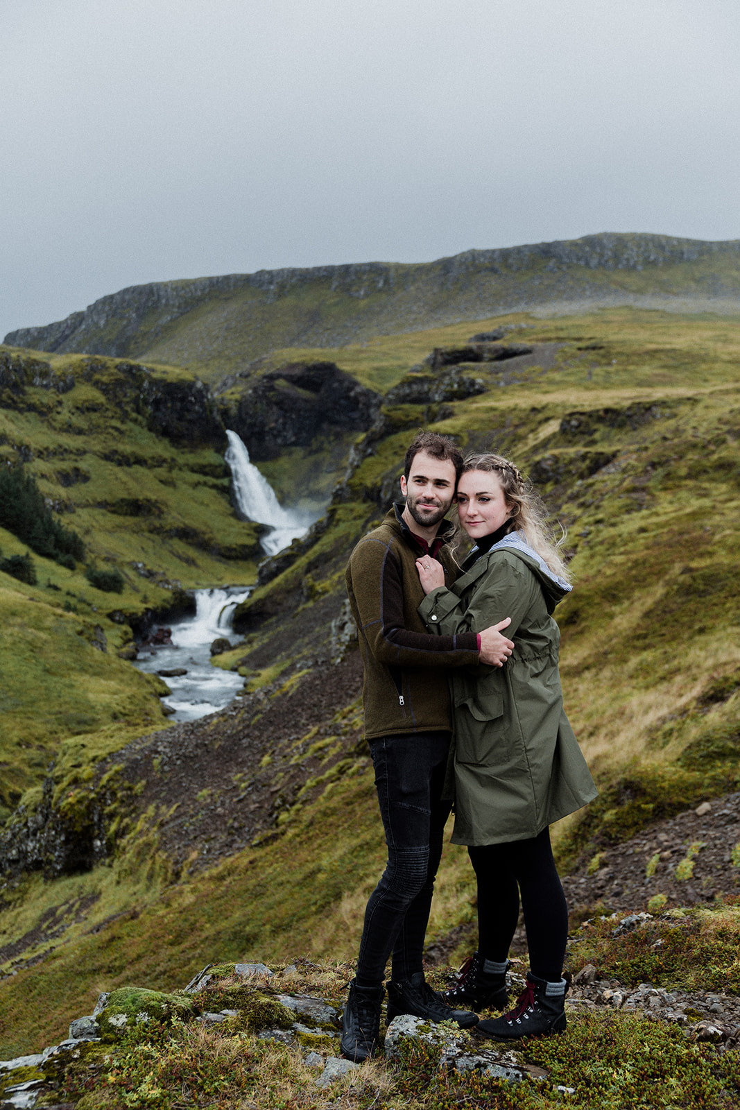 A couple standing in front of a stunning waterfall enjoying an adventure session photography in Iceland