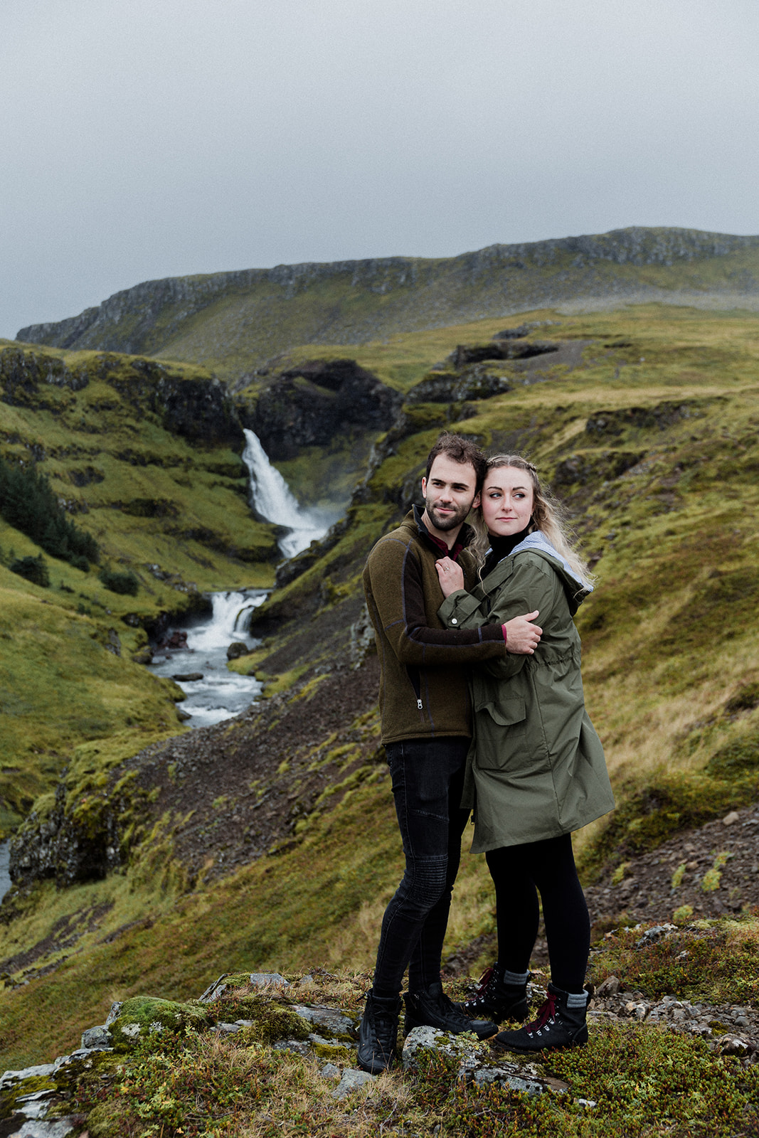 A couple standing in front of a stunning waterfall enjoying an adventure session photography in Iceland