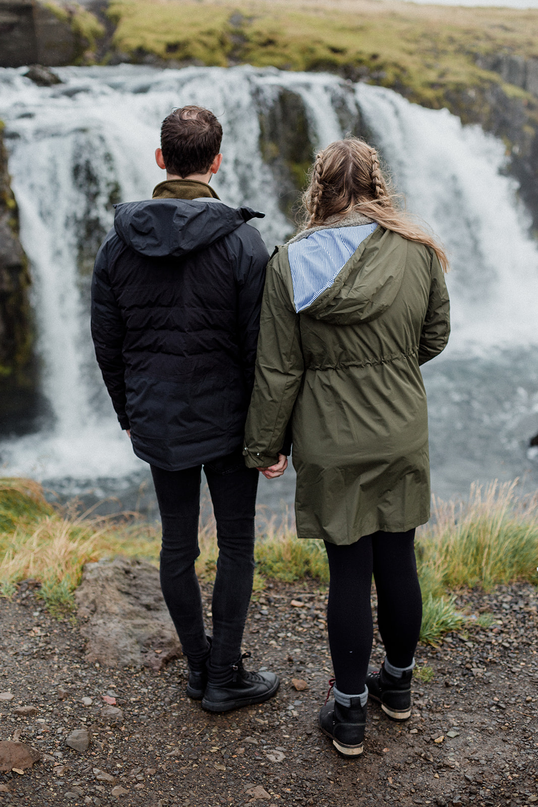 A couple standing in front of the stunning Kirkjufellsfoss waterfall enjoying an adventure session in Iceland