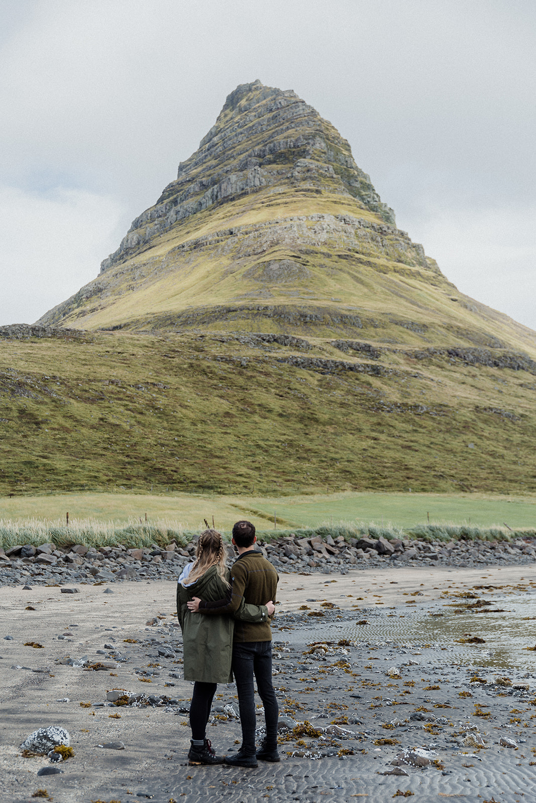 A couple standing in front of the stunning Mt. Kirkjufell enjoying an adventure session photography in Iceland