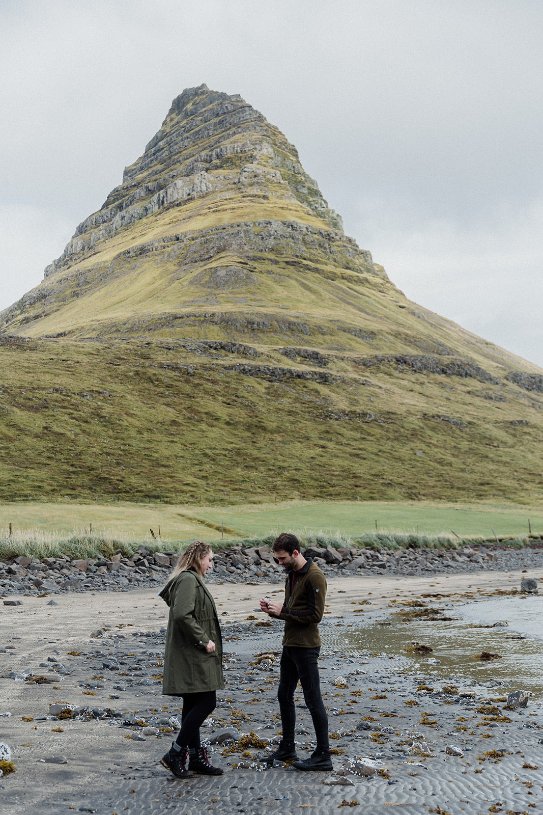 A couple standing in front of the stunning Mt. Kirkjufell enjoying an adventure session photography in Iceland