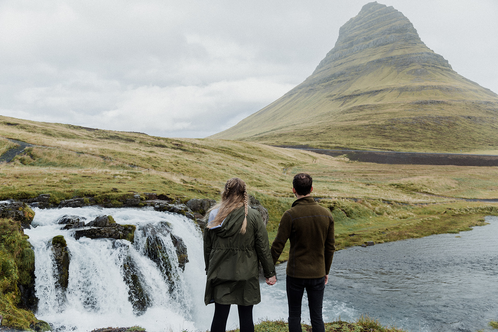A couple standing in front of the stunning Mt. Kirkjufell and Kirkjufellsfoss waterfall enjoying an adventure session