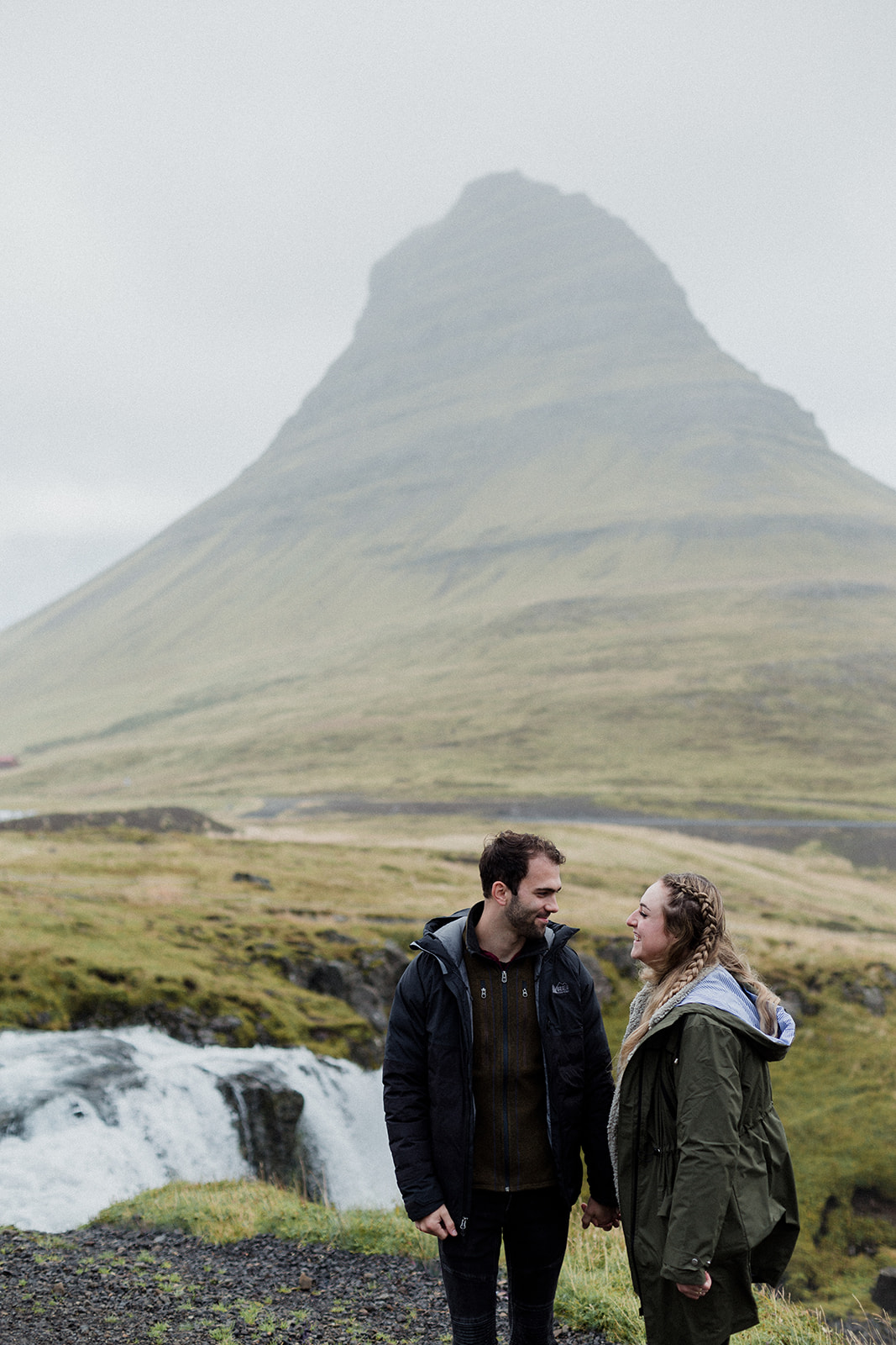 A couple standing in front of the stunning Mt. Kirkjufell and Kirkjufellsfoss waterfall enjoying an adventure session