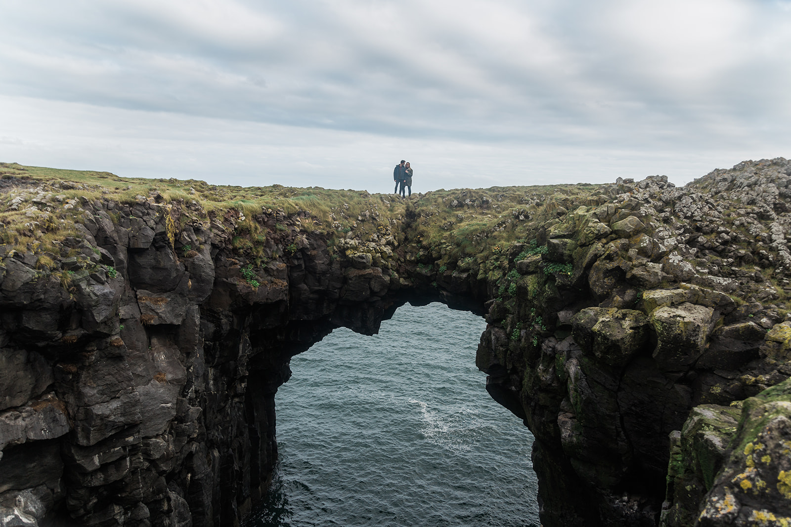 A couple standing on the volcanic rock bridge at the Gatklettur Cliff walk, Arnarstapi, Snæfellsnes Peninsula, Iceland