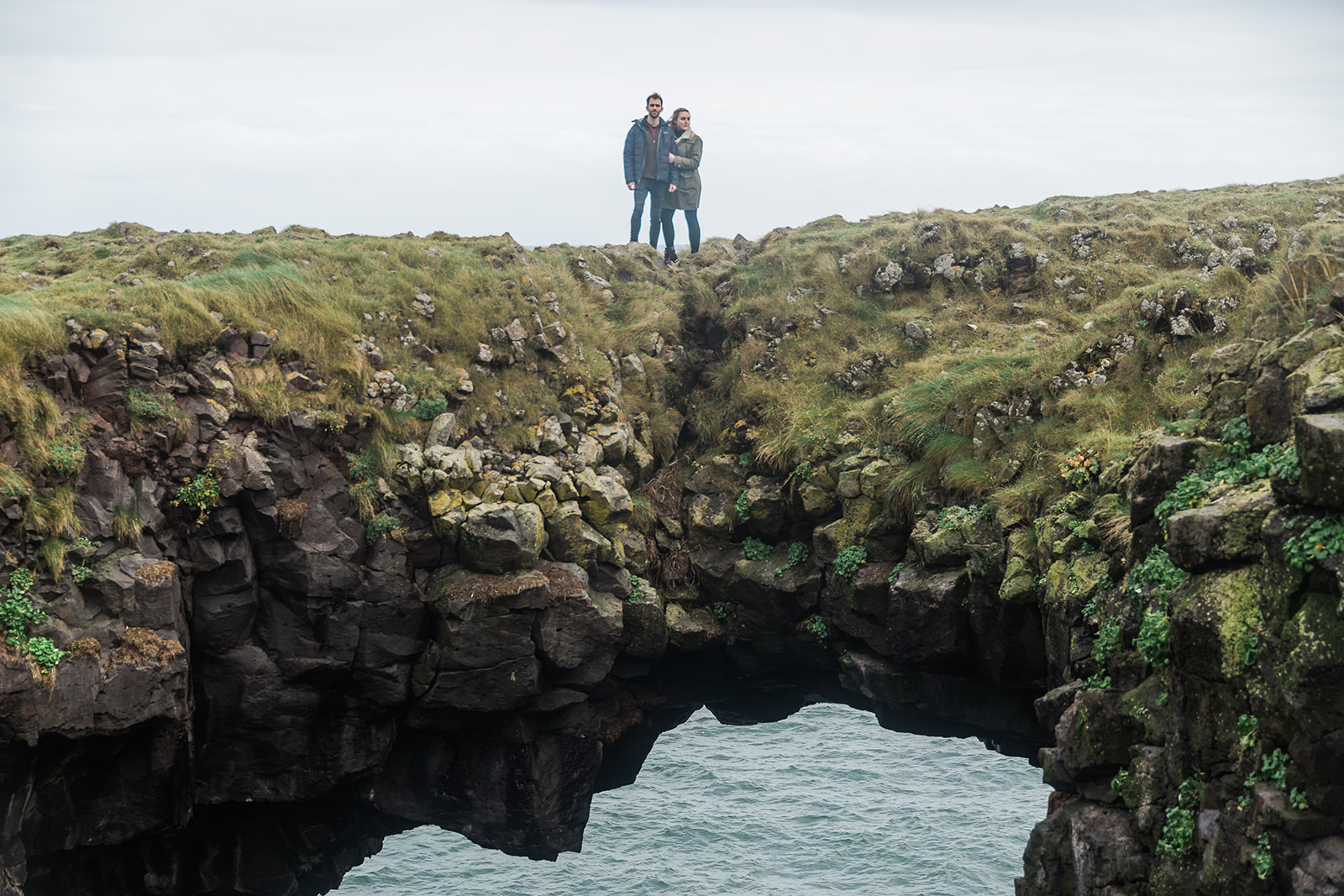 A couple standing on the volcanic rock bridge at the Gatklettur Cliff walk, Arnarstapi, Snæfellsnes Peninsula, Iceland