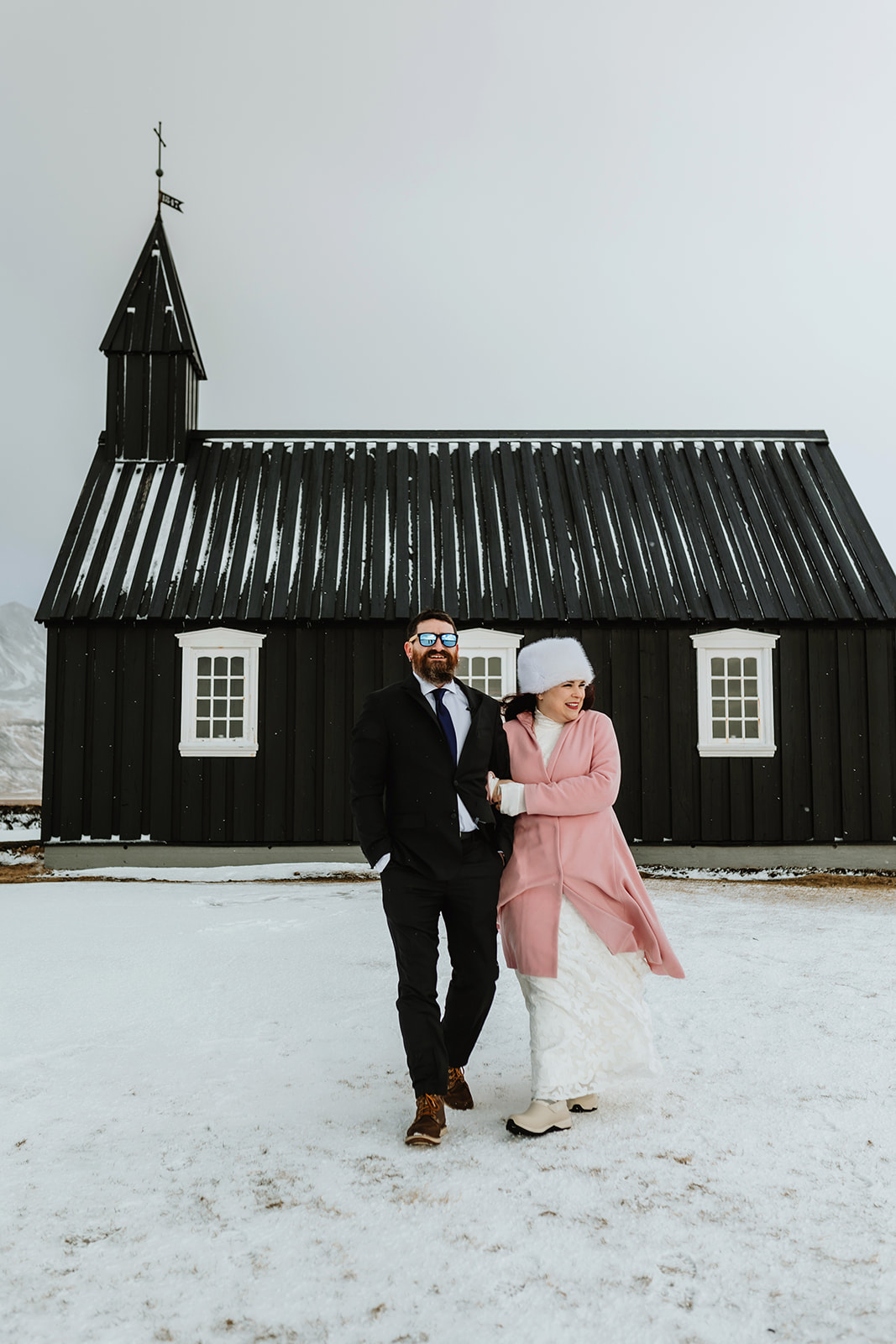 Married couple who eloped in Iceland are standing in front of the black church after their wedding ceremony 