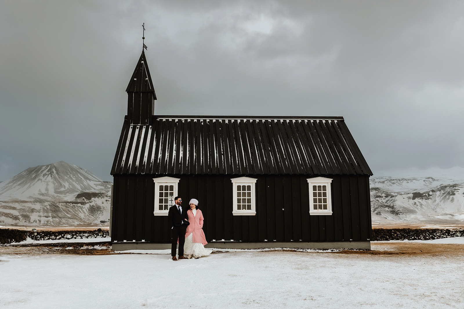 Married couple who eloped in Iceland are standing in front of the black church after their wedding ceremony 
