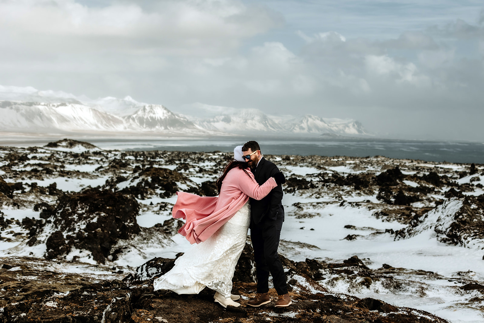 Married couple who got married in Iceland are standing on top of a mountain and surrounded by snow and mountains
