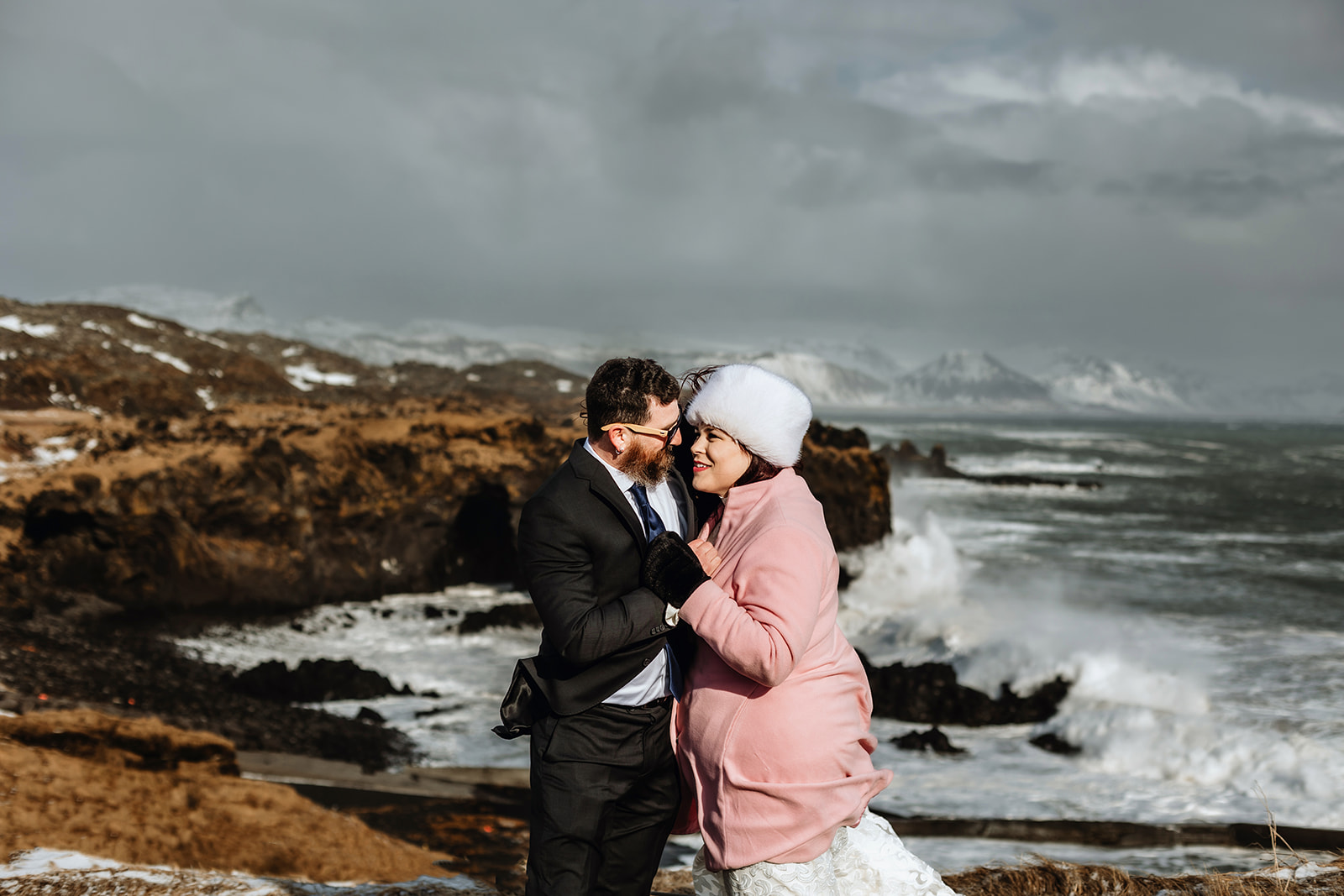 Married couple is hugging in front of a stormy Ocean in Iceland on their weddign day
