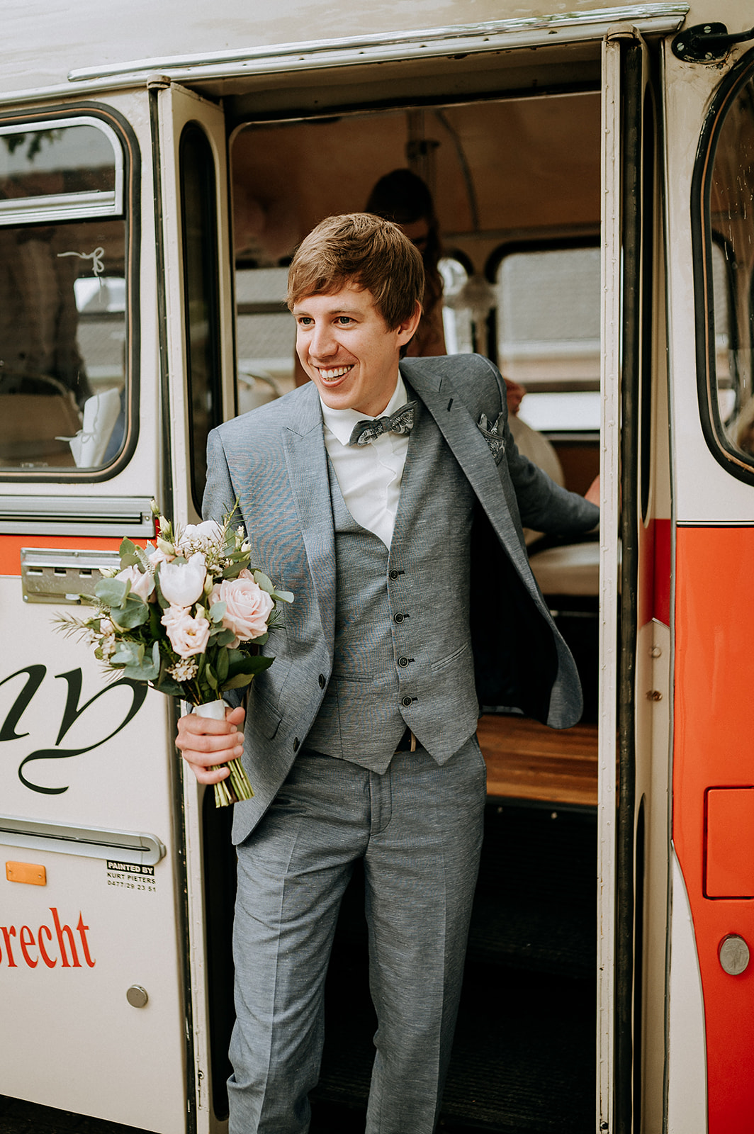 Bruidegom stapt met het bruidsboeket van de mooi versierde bus.