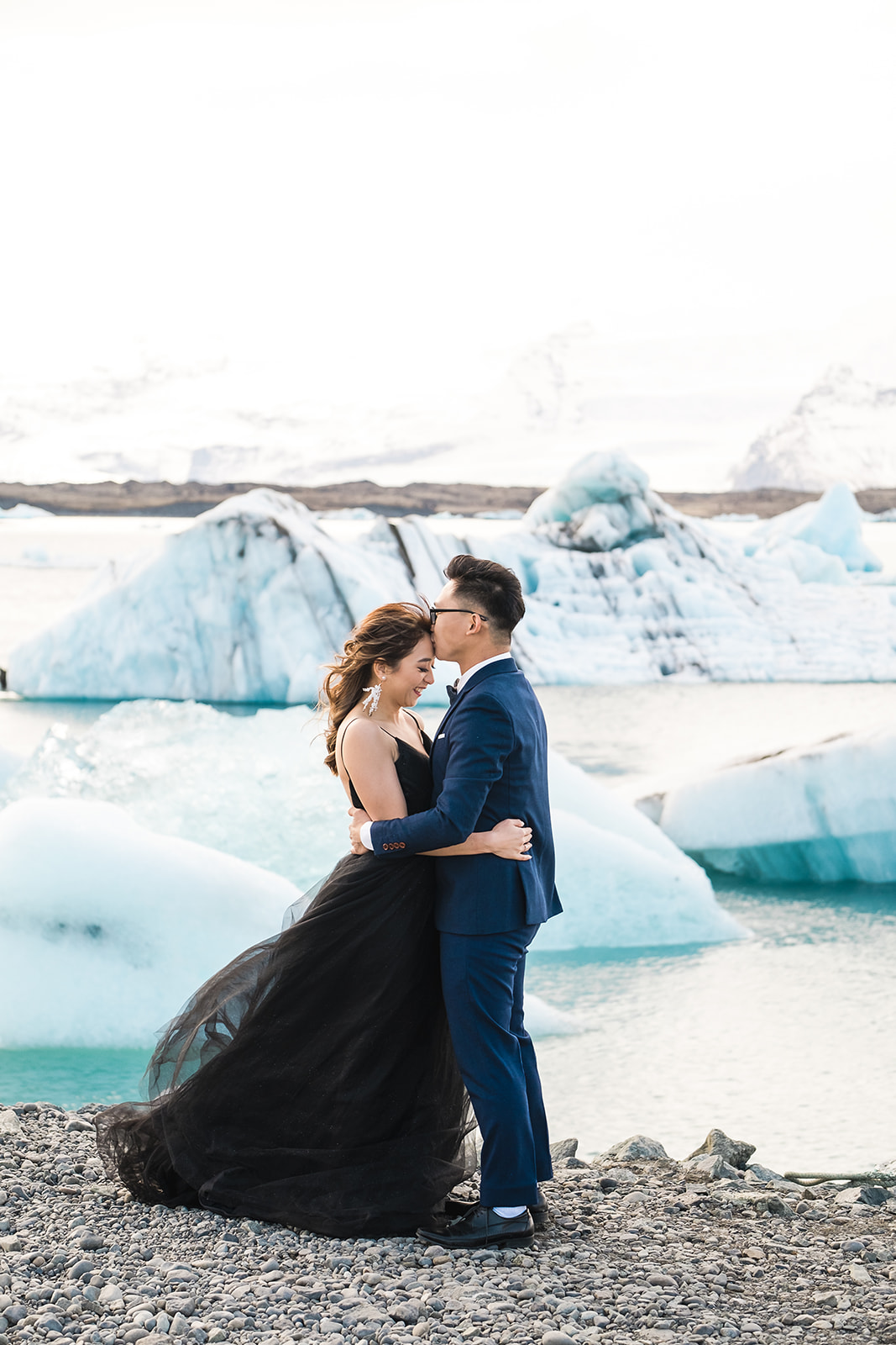 A couple standing in front of Icebergs Pre-wedding Adventure Session at Jökulsárlón Glacier Lagoon Iceland black dress