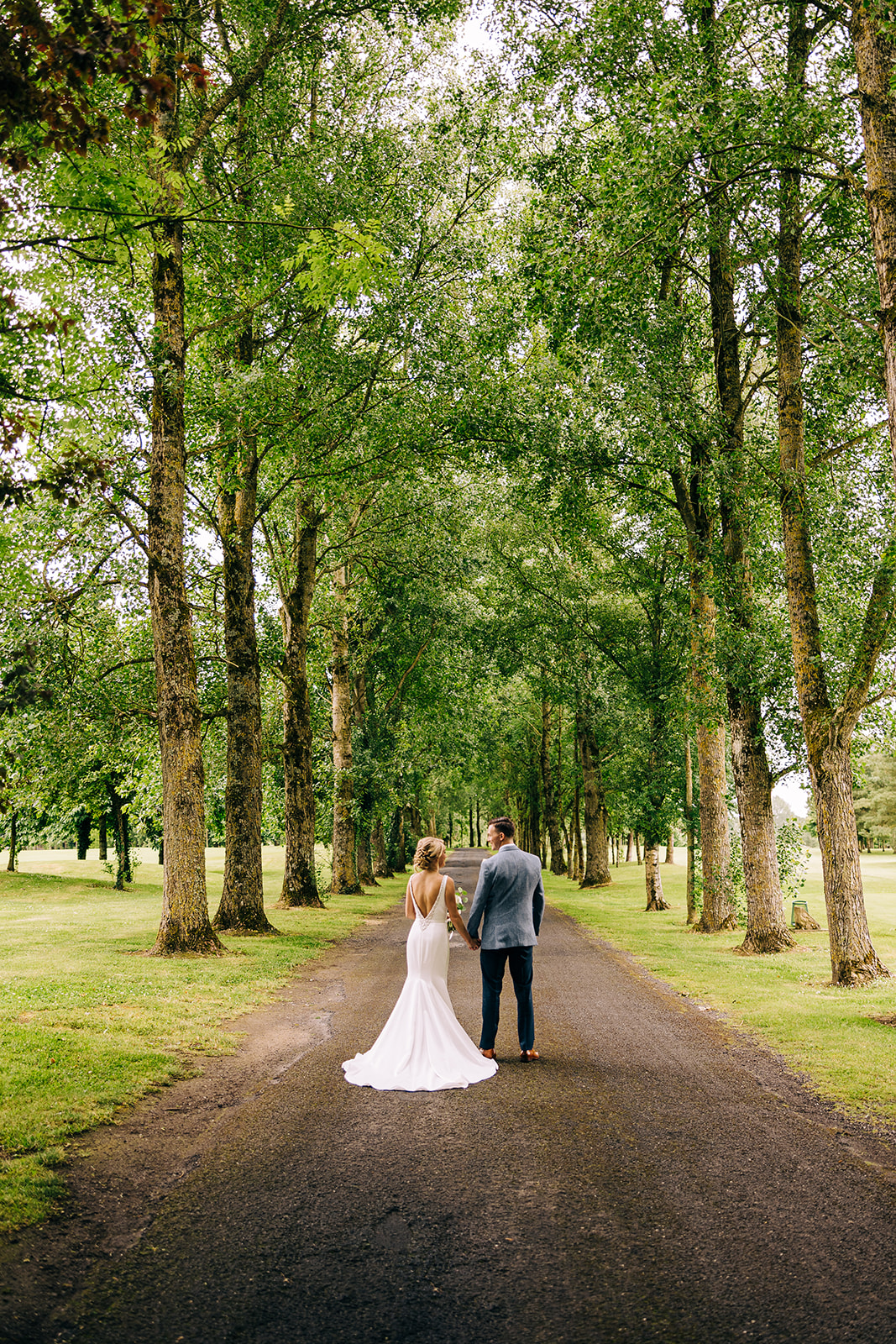 A bride and groom walk down kilkea's castle tree lined driveway