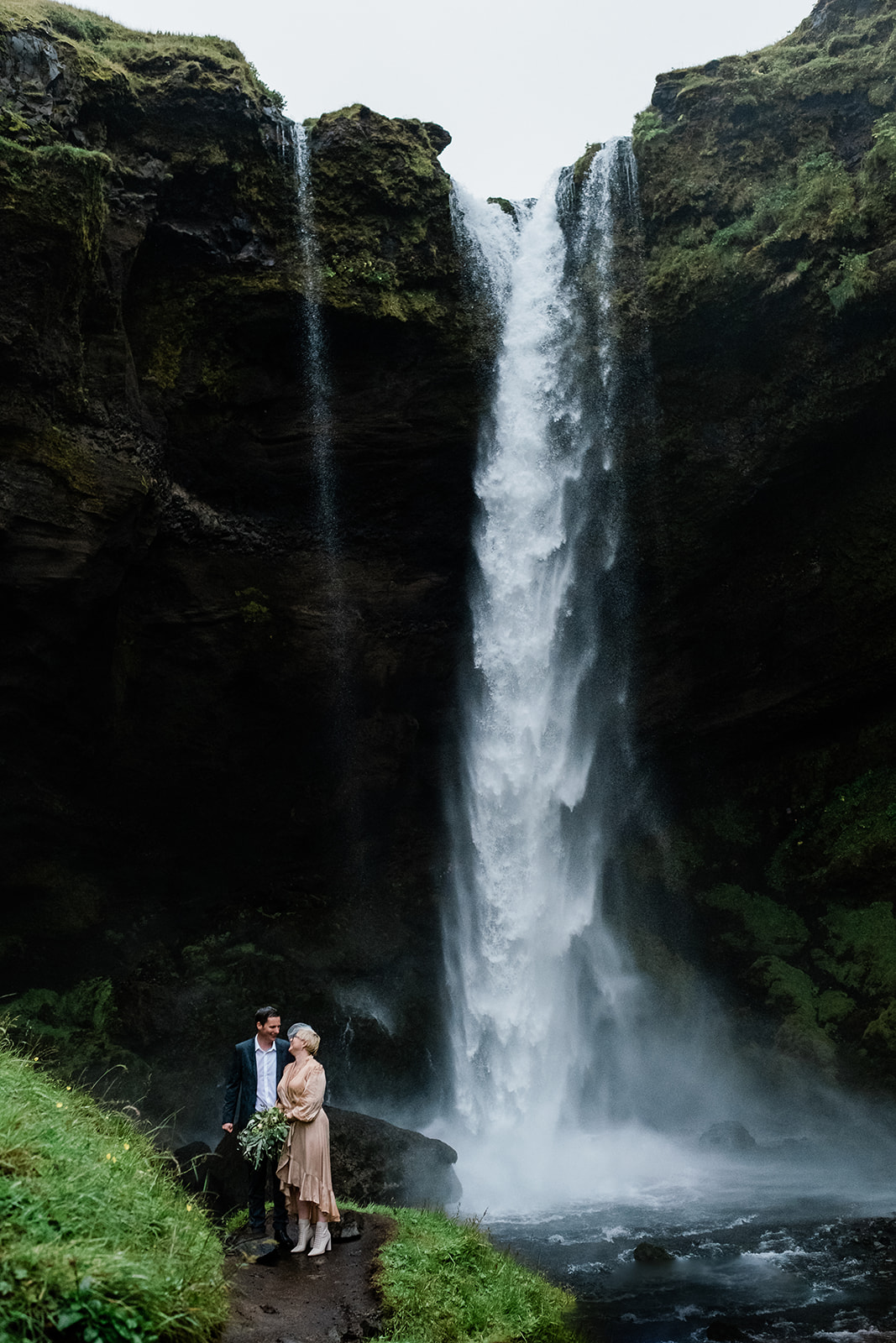 A couple standing under the rain in front of Kvernufoss Waterfall in Iceland