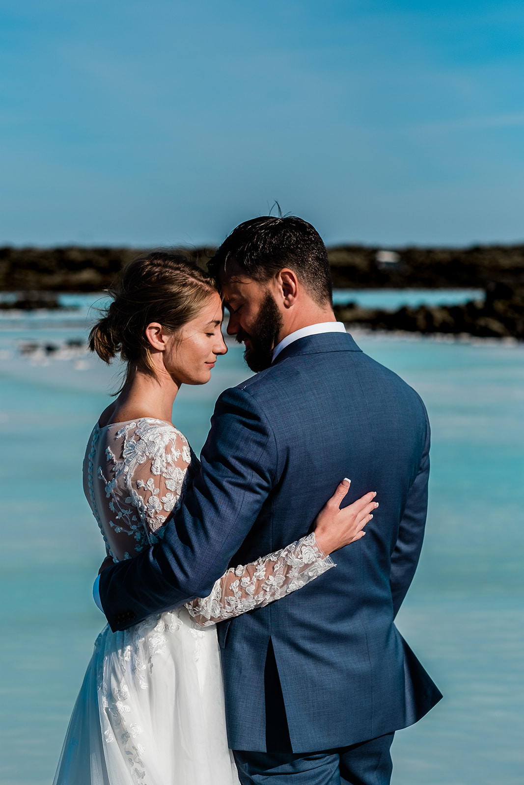 A stunning couple standing and hugging at the Blue Lagoon during their Ethereal Summer Elopement at Reykjanes Peninsula