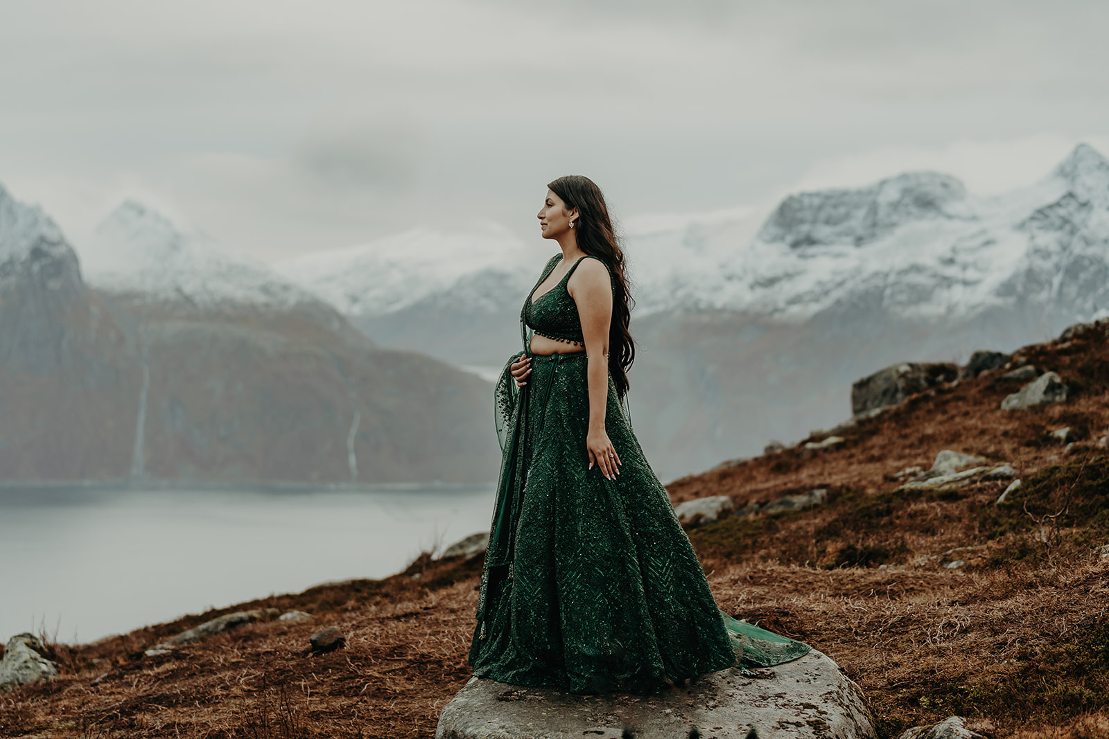 Woman dressed in traditional clothes holding hands on top of a mountain in senja. 
