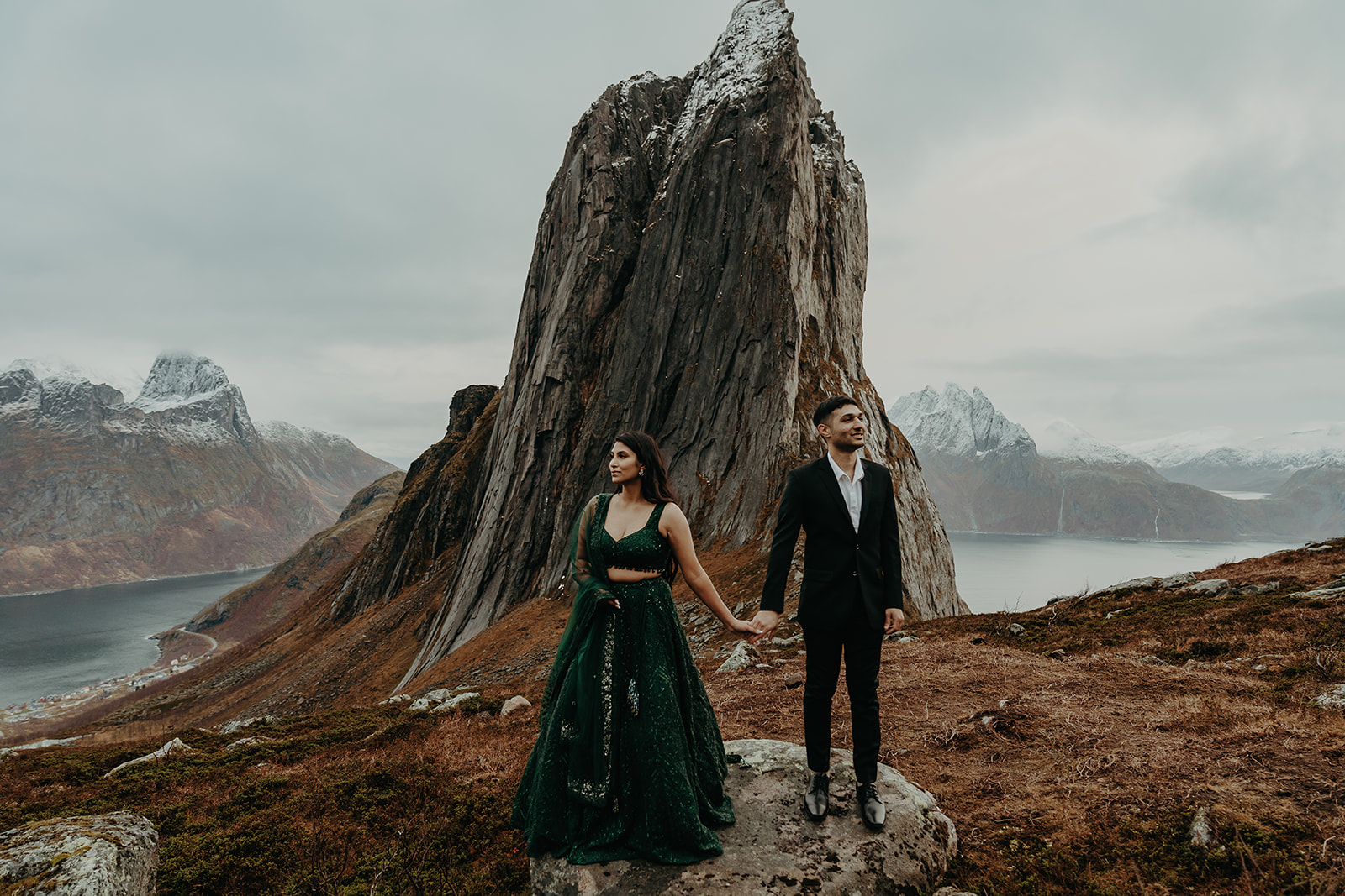 Couple dressed in traditional clothes holding hands on top of a mountain in senja. 