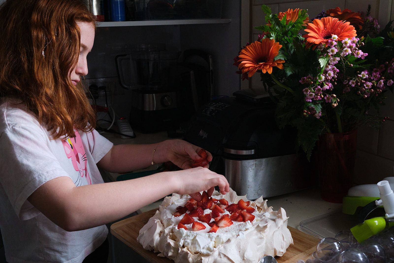 a girl arranging strawberries on a cake in the kitchen with flowers