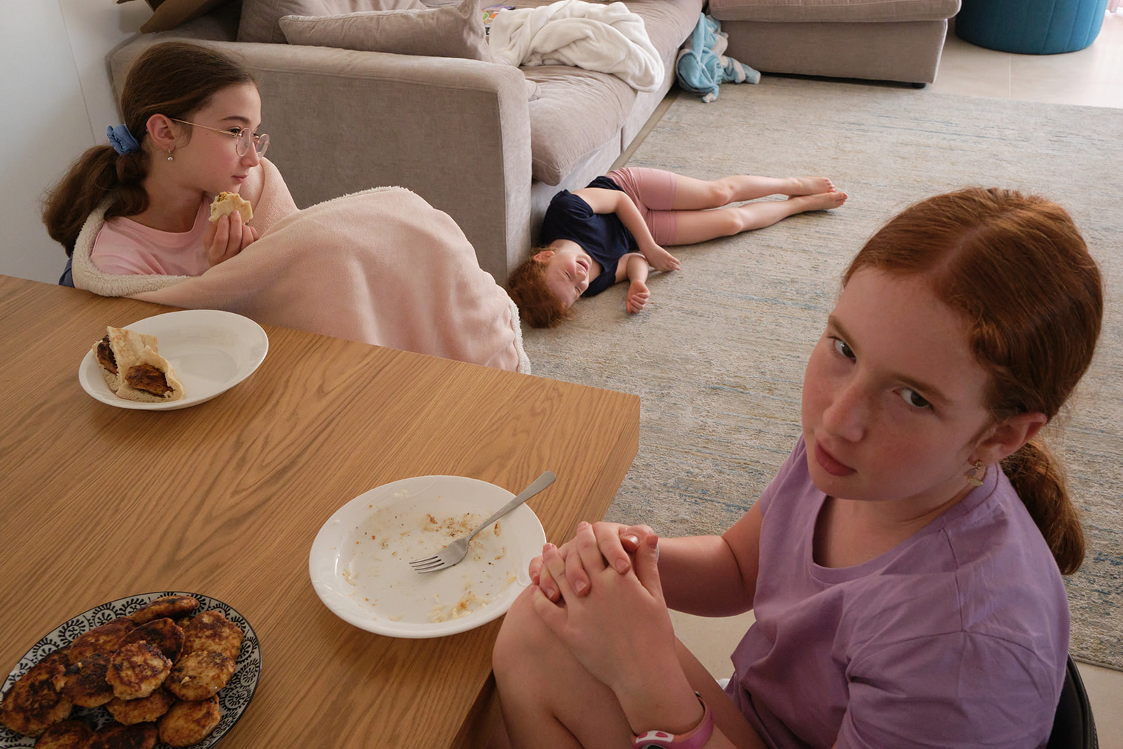 a girl laughing on the floor while her sisters sit at the table 
