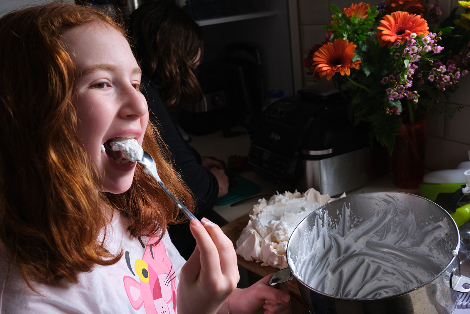 a girl licking cake batter off a spoon in the kitchen with flowers