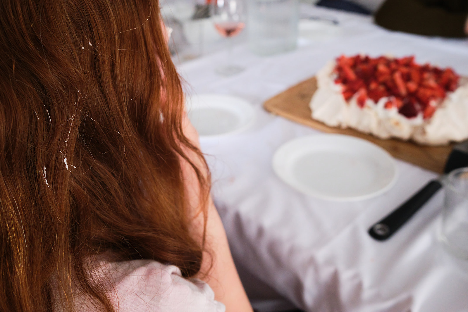 a girl sitting at the table in front of a strawberry cake with whipped cream in her hair