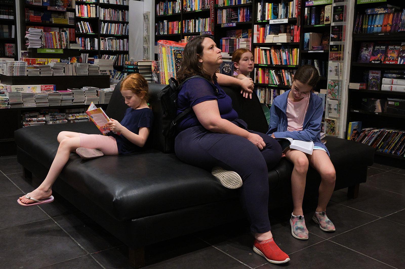 a mother and three girls sitting on a couch in a book shop reading
