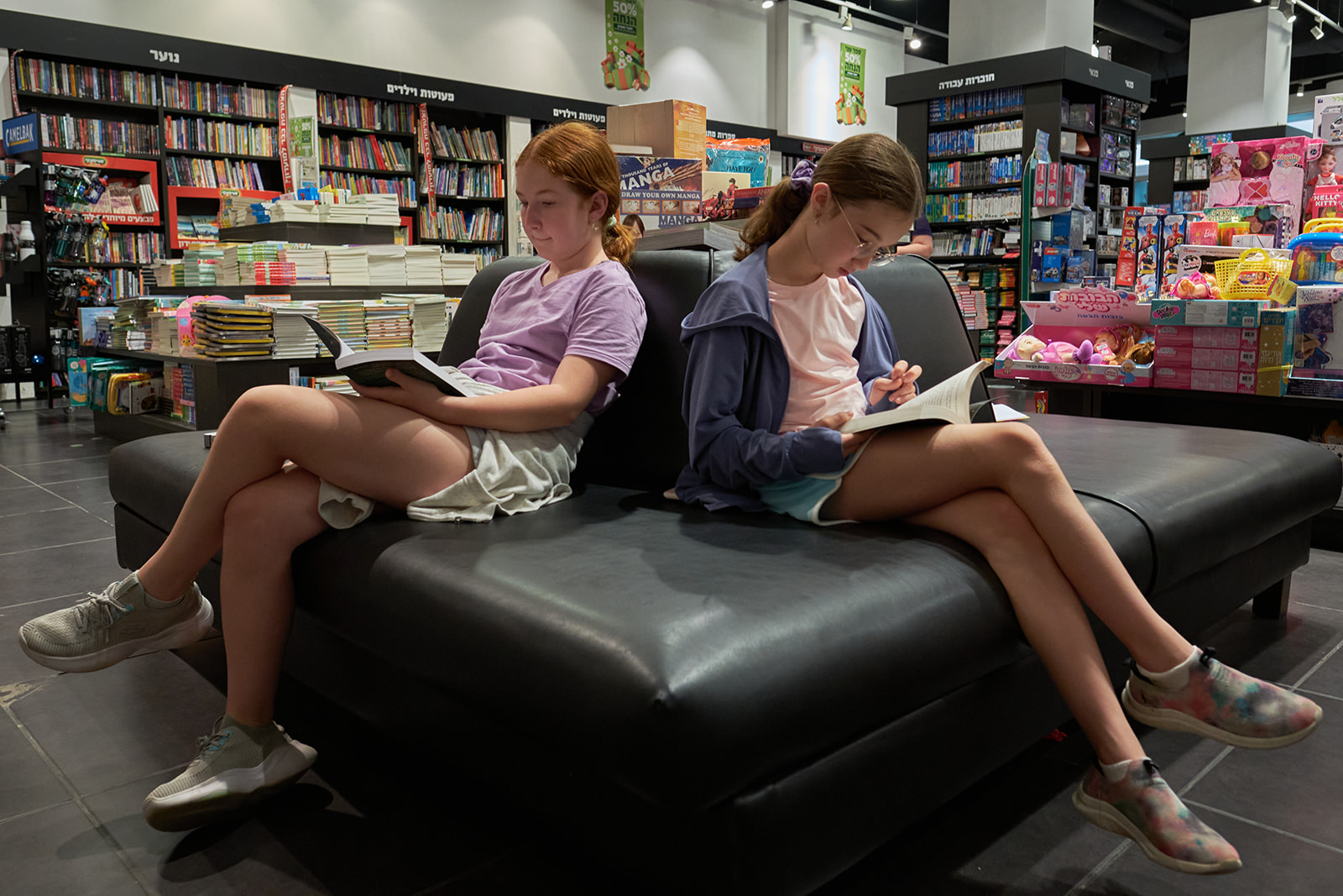 two girls sitting on a couch in a book shop reading