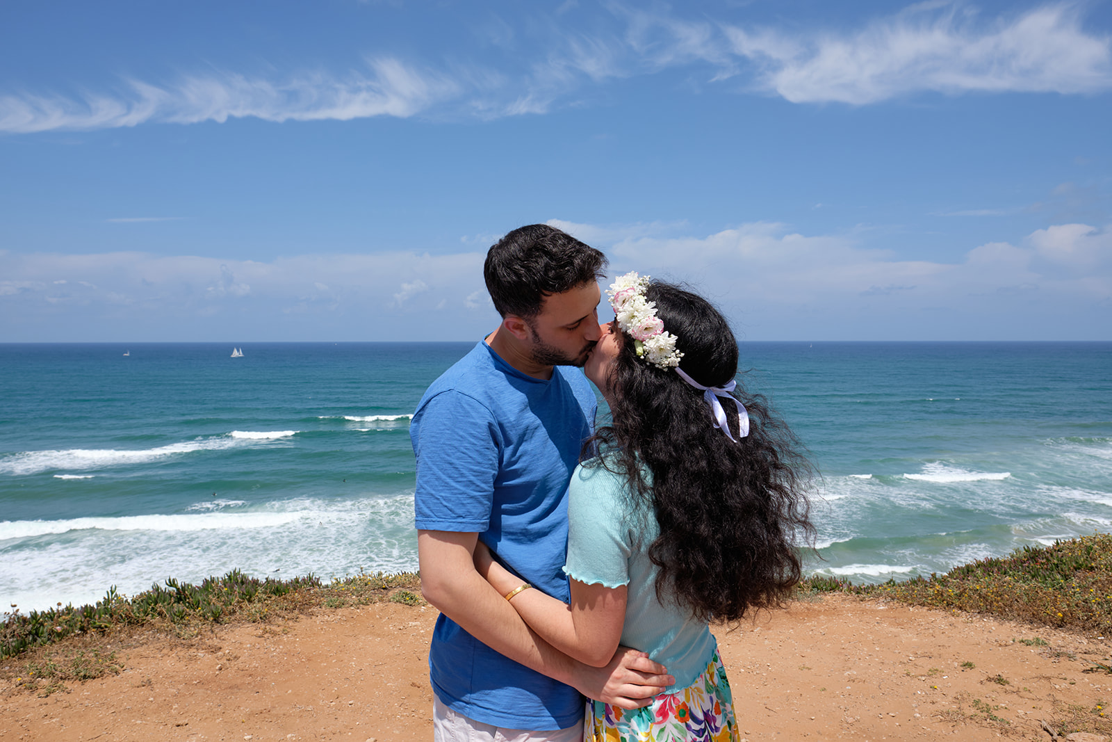 engaged couple kissing and hugging by the beach flowers in her hair