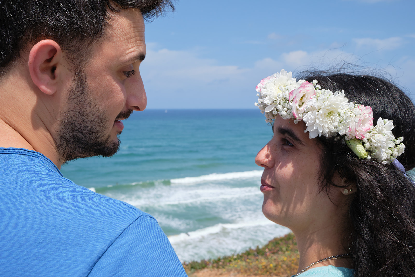 engaged couple looking at each other by the beach flowers in her hair
